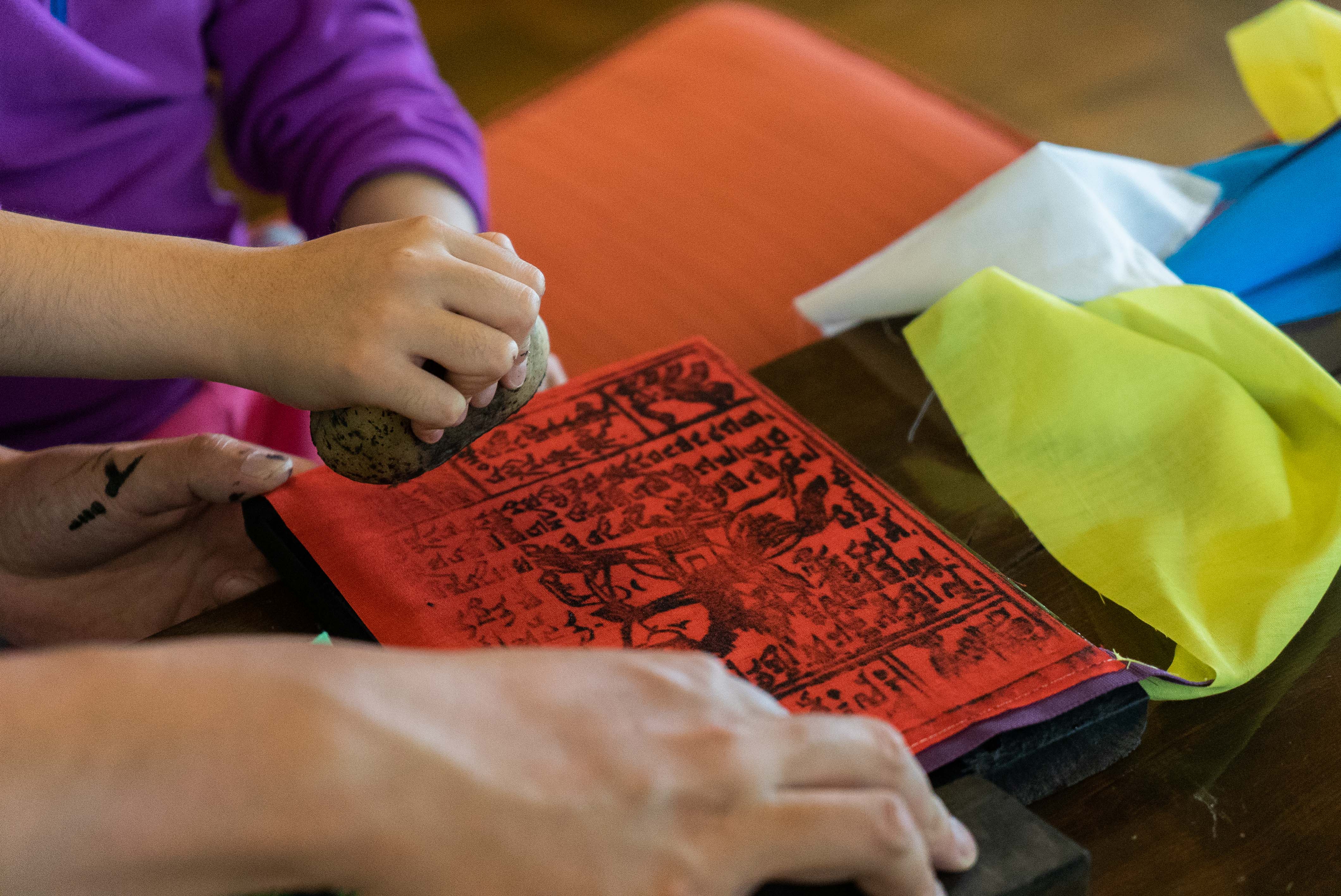 Hands printing a red windhorse prayer flag from a carved woodblock