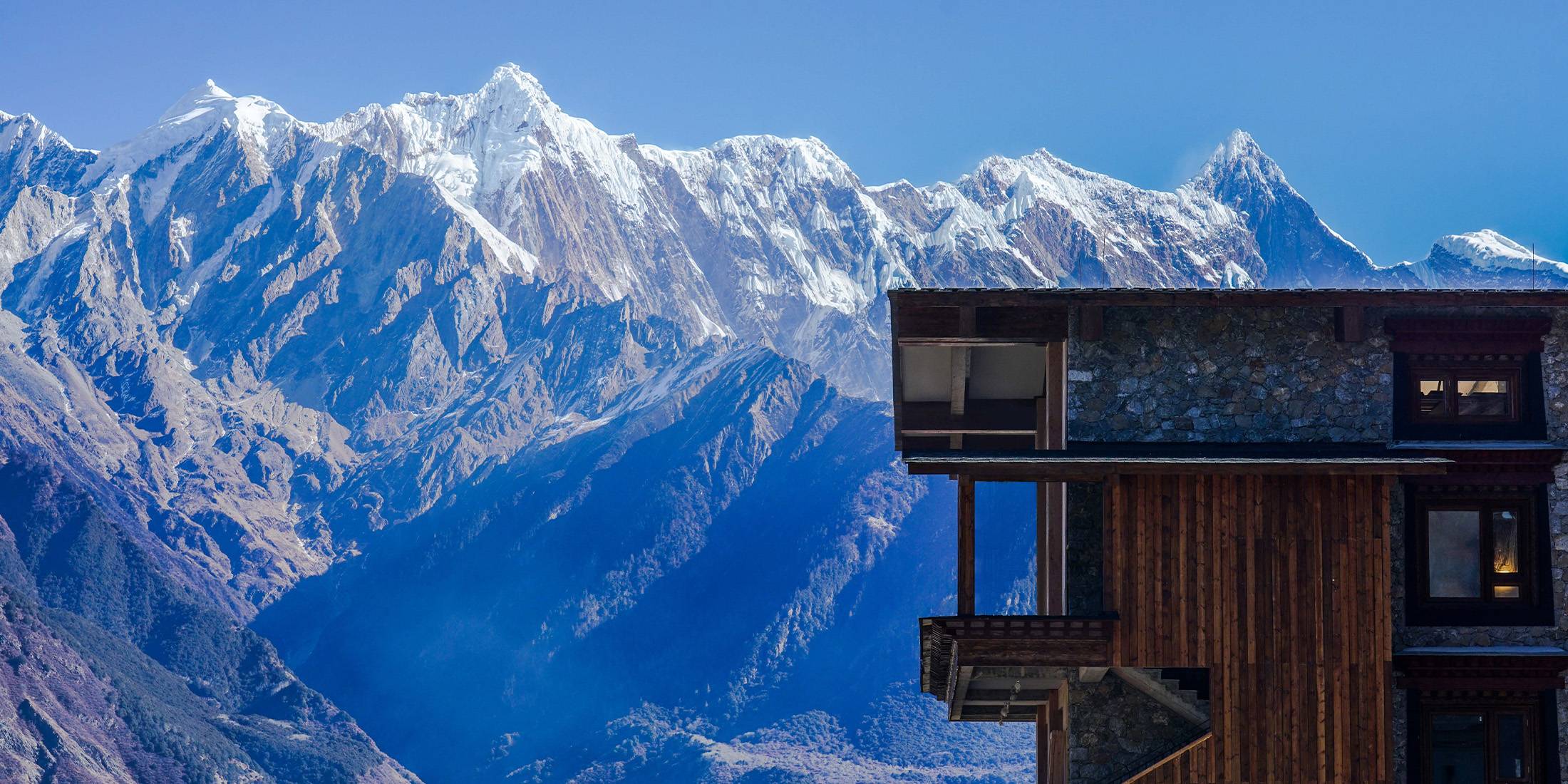 Songtsam Namcha Barwa Lodge silhouetted against a wall of snow peaks